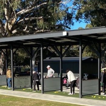 New golfers try out their swing at the driving range while their coach watches attentively